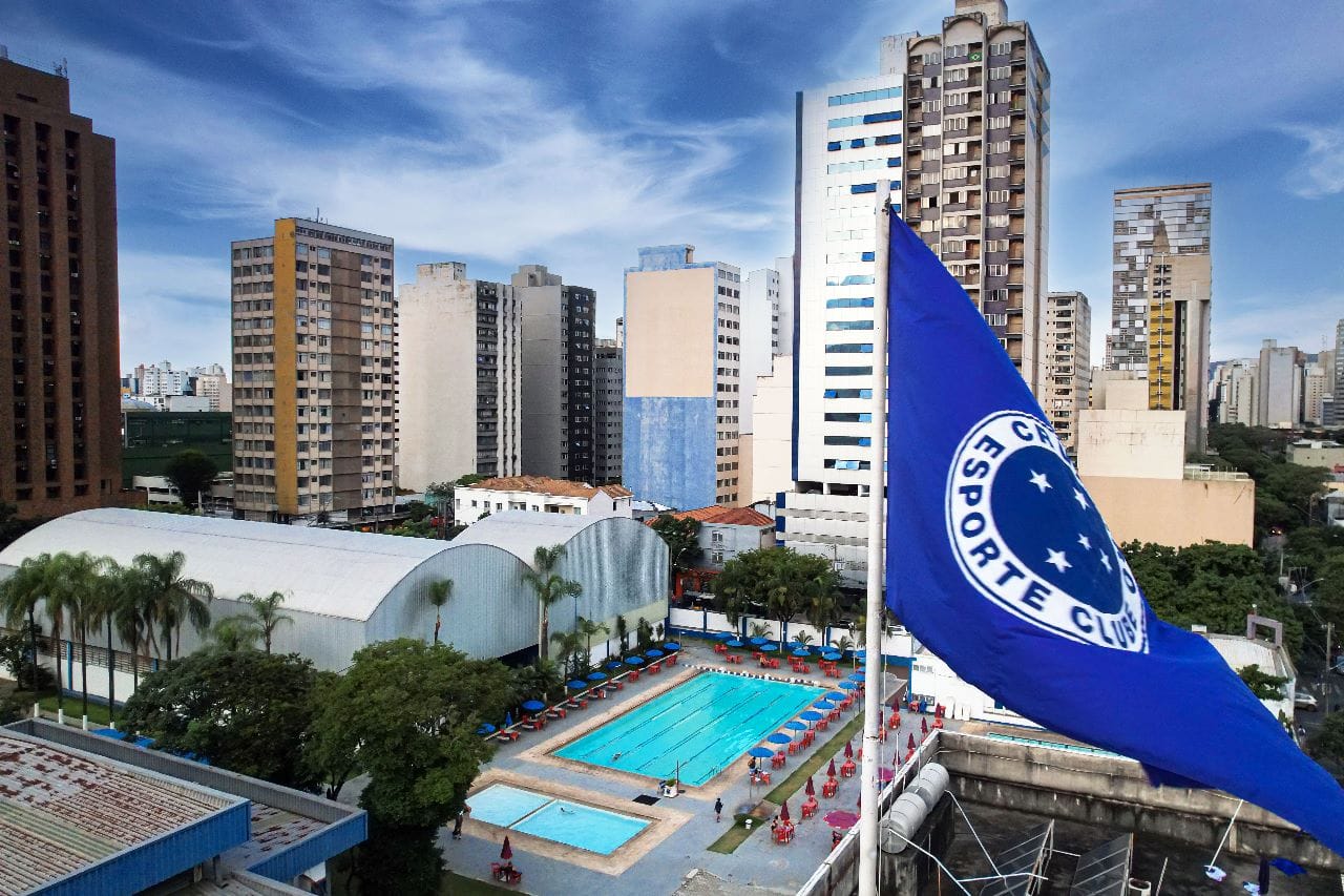 Vista do clube Cruzeiro com bandeira azul e prédios ao fundo em Belo Horizonte